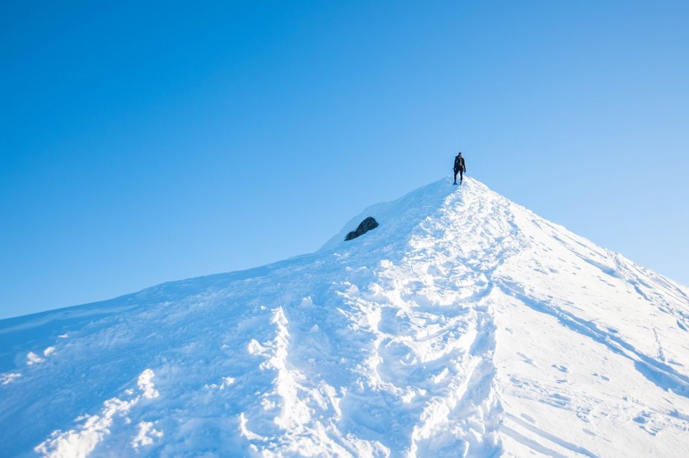 Person,Clibming,Up,Snowy,Mountain,Peak.,Blue,Sky,In,Afternoon.