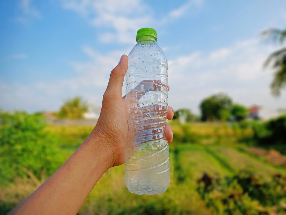 Hand,Holding,Water,Bottle,With,Blurry,Background,Of,Blue,Sky