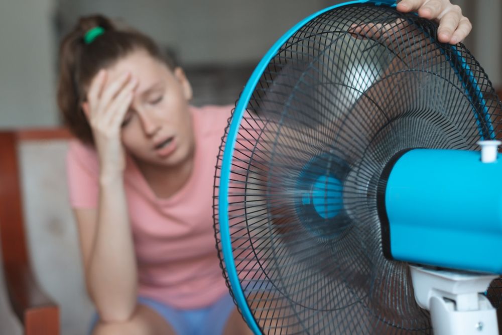 Young,Woman,Using,Electric,Fan,At,Home,In,Living,Room,