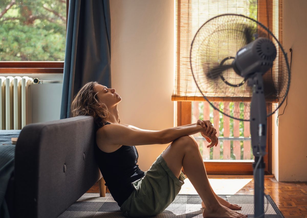 Meleg időjárás miatt szenvedő nő a ventilátor előtt.